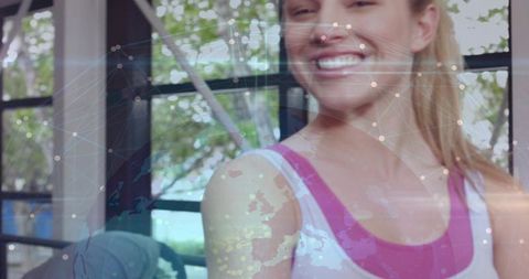 Smiling woman standing in fitness studio with global map network overlay and natural light