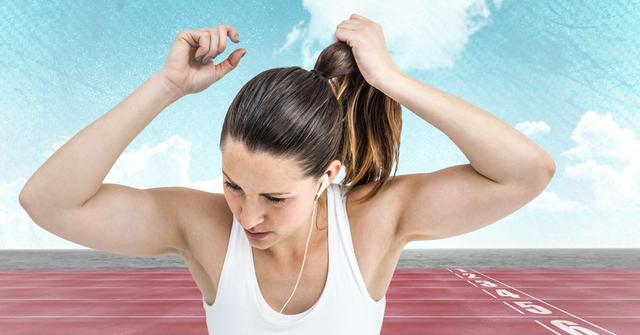 Young female athlete preparing for a race by tying her hair on a running track, with clear sky backdrop. Ideal for use in fitness, sports marketing, motivational posters, athletic event promotions, and health-related content.