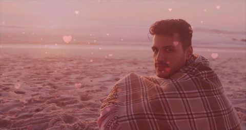 Man Wrapped in Plaid Blanket on Sandy Beach at Sunset