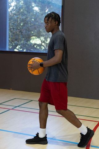 African american man dribbling basketball on indoor hardwood court wearing smartwatch