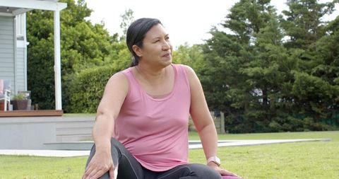 Mature woman sitting on yoga mat in backyard resting after workout wearing fitness tracker