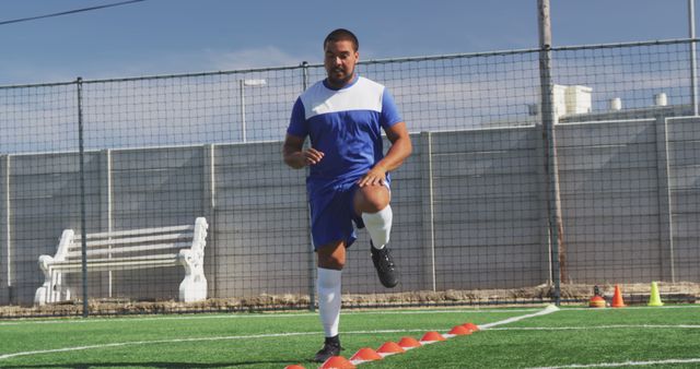 Biracial male football player wearing blue uniform training on outdoor pitch. Football, sports and fitness.