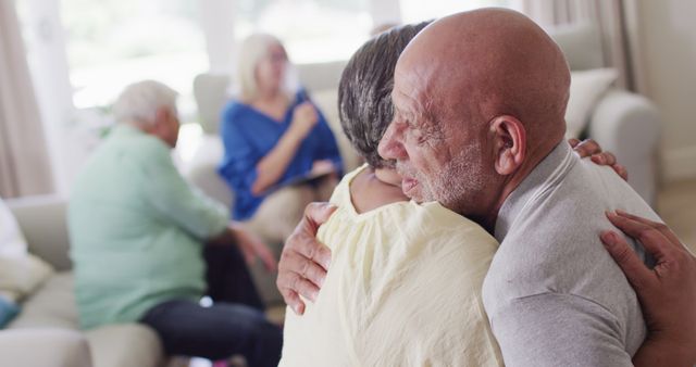 Senior couple embracing during a group therapy session, showing emotional support and connection. Ideal for advertising mental health services, elderly care facilities, support groups, and community therapy programs. Use in brochures, websites, or social media posts to highlight emotional bonds and support systems for elderly individuals.