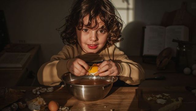 Curly-Haired Child Cracking Egg Into Steel Mixing Bowl While Baking on Sunlit Countertop