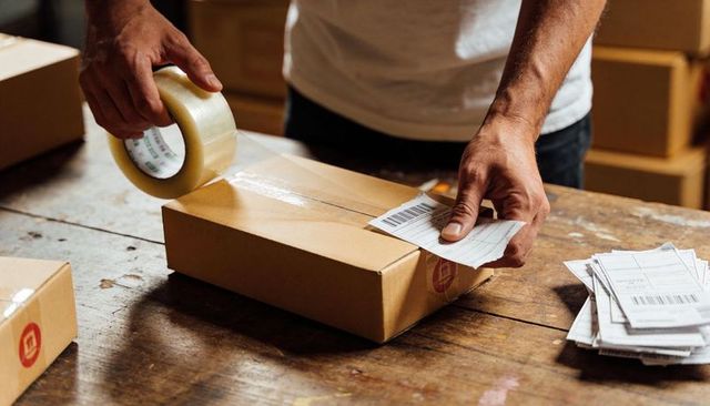 Warehouse worker taping shipping box and applying barcode label at fulfillment workstation