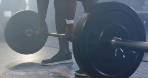 African man gripping loaded barbell and preparing deadlift on gym rubber floor