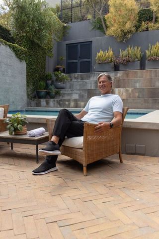 Relaxing senior man lounging on wicker armchair beside pool in contemporary backyard terrace