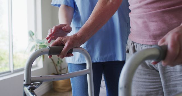 An elderly individual receiving help from a caregiver while using a walker indoors. This image highlights the importance of support and assistance for those with limited mobility. It can be used for educational materials, healthcare websites, brochures on elderly care services, or promotions for home care agencies.