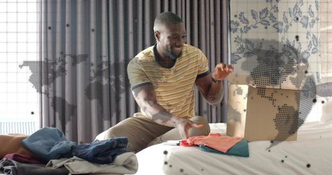 Smiling man sorting folded t-shirts on bed, packing boxes and organizing wardrobe at home