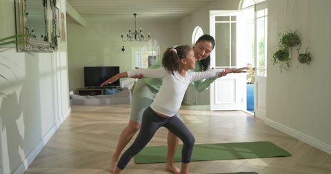 Woman teaching child standing yoga pose in sunlit living room, home fitness posture