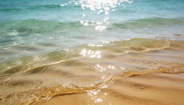 Sunlit shallow seawater lapping golden rippled sand with turquoise waves shimmering