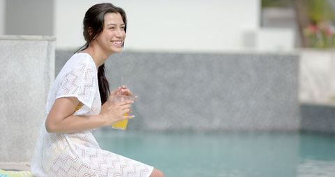 Smiling woman relaxing by poolside with refreshing drink