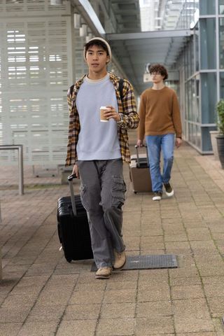 Young travelers walking through transit hub pulling suitcases and holding takeaway coffee