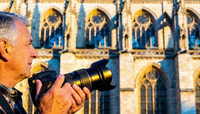 Senior photographer aiming dslr with telephoto lens at gothic cathedral facade in golden light