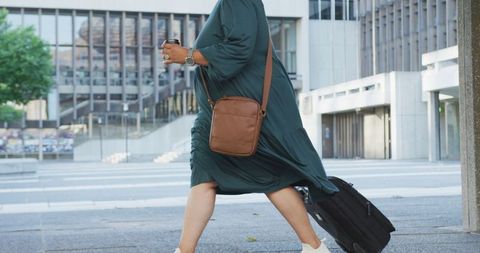 Confident Woman Walking with Luggage and Coffee in Modern Cityscape