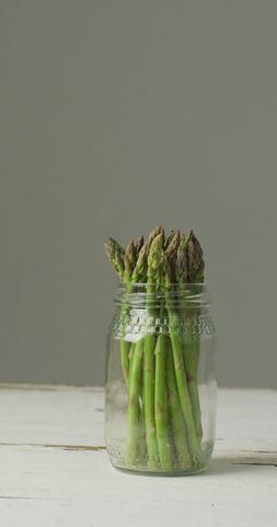 Fresh Asparagus in Glass Jar on Neutral Background