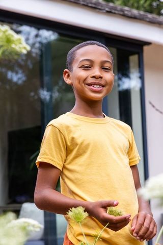 African american preteen smiling in garden wearing yellow tee holding green seedheads