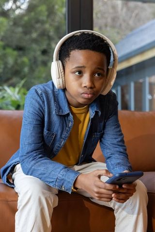 Preteen african american boy listening to music with headphones using smartphone on couch