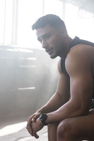 Muscular man resting between workouts in sunlit gym wearing fitness tracker