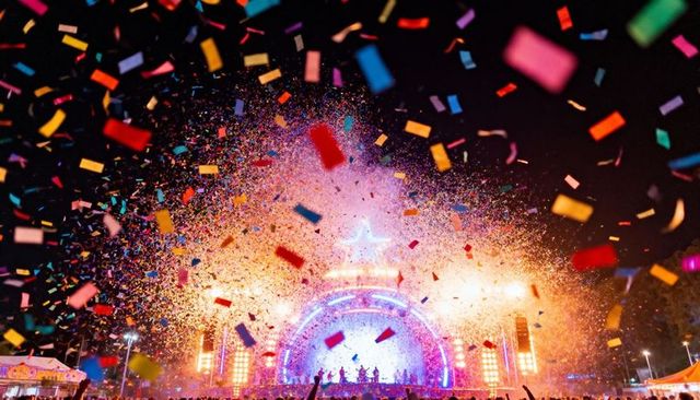 Confetti exploding over star-arched neon stage at outdoor night festival concert