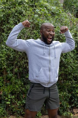 African american man flexing and laughing outdoors in gray hoodie and shorts celebrating
