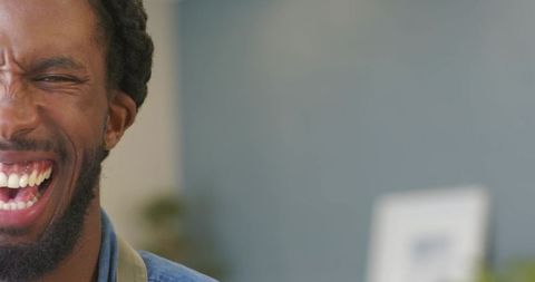 African american man laughing candidly in kitchen wearing denim shirt and apron strap