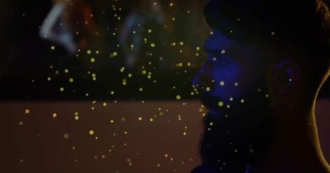 Introspective bearded man observing ambient gold particles in studio