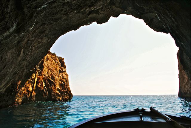 Boat entering sunlit sea cave with blue ocean beyond. Ideal for travel blogs, adventure themes, exploration articles, and nature documentaries. Perfect for promoting coastal tourism and maritime activities.