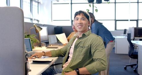 Young professional smiling in open-plan office with diverse team collaborating on paperwork