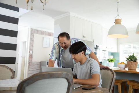 Father guiding son on laptop at home kitchen table