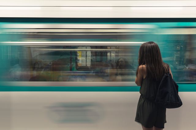 This visual captures a woman with backpack waiting for fast moving train in urban metro station. Excellent for illustrating urban life, commuting scenarios, transportation articles or in travel-related content to depict public transport in city environments.