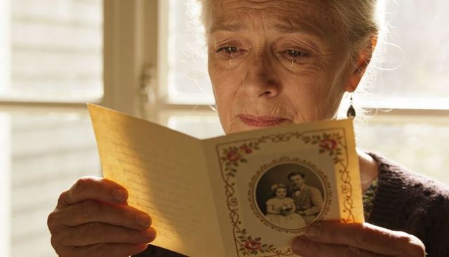 Senior woman reading vintage family card crying with tears feeling nostalgic