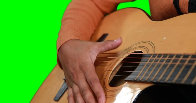 This image of a person playing an acoustic guitar with a green screen background can be used for music-related projects, instructional materials, or in digital compositions where the background can be easily altered. Great for educational content about learning to play guitar, music videos, or advertising for music products and services.