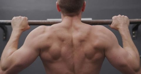 Athletic man performing chin ups in gym close-up