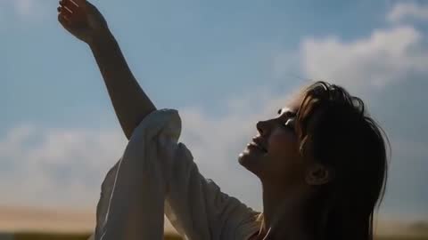 Woman raising arm and smiling toward sky at golden hour over open field, silhouette