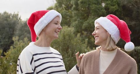 Senior and middle-aged women chatting in garden wearing santa hats sharing holiday cheer