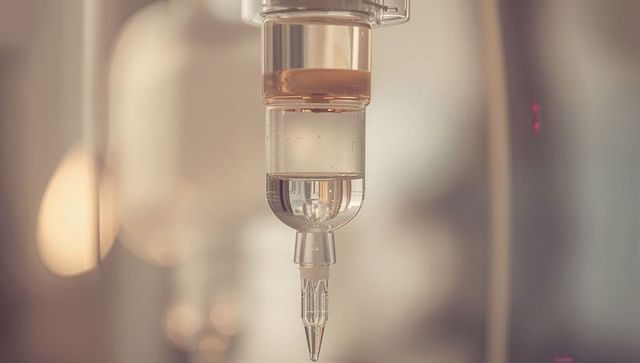 Iv drip chamber showing amber adapter and tubing with soft bokeh hospital background