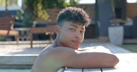 African american young man leaning on pool edge relaxing in sunlit backyard patio