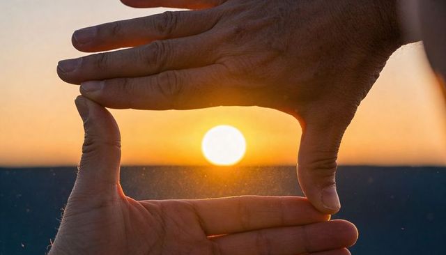 Hands framing sun at golden sunset creating natural frame and silhouette glow
