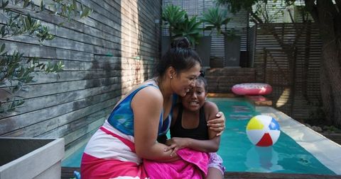 Mother and daughter bonding by backyard pool with beach ball