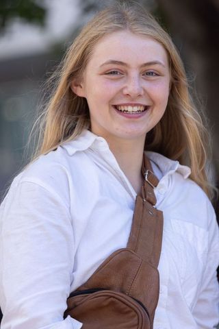 Smiling teen student on campus wearing white shirt and brown leather sling bag
