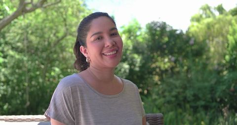 Smiling woman relaxing on patio chair in sunlit garden wearing gray t-shirt