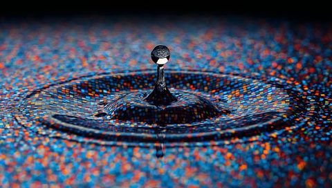 Rebounding Water Droplet Reflecting Vibrant Pixel Mosaic on Rippled Liquid Surface