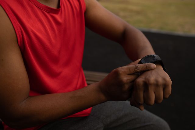 Mid section of biracial man wearing sportswear checking his smartwatch, taking a break from running workout. Fitness outdoor healthy lifestyle.