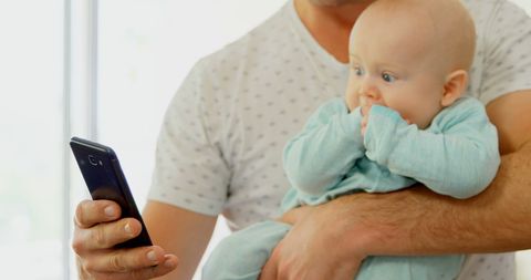 Father Holding Baby While Checking Smartphone with Copy Space