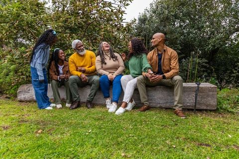 Laughing african american multigenerational family connecting on log bench park outing