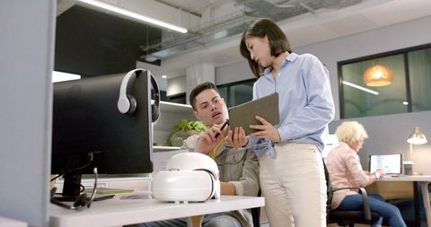Colleagues collaborating over tablet in modern open office with VR headset