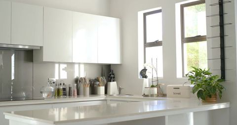 Sunlit Minimalist White Kitchen with Glossy Island Reflecting Light and Organized Details