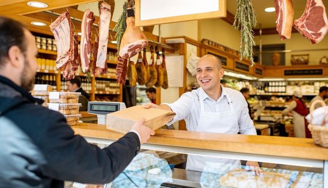 Smiling butcher handing brown paper bag to customer at rustic deli counter