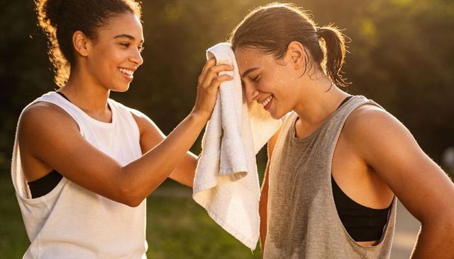 Partners cooling down after workout wiping sweat with towel during golden-hour outdoor fitness